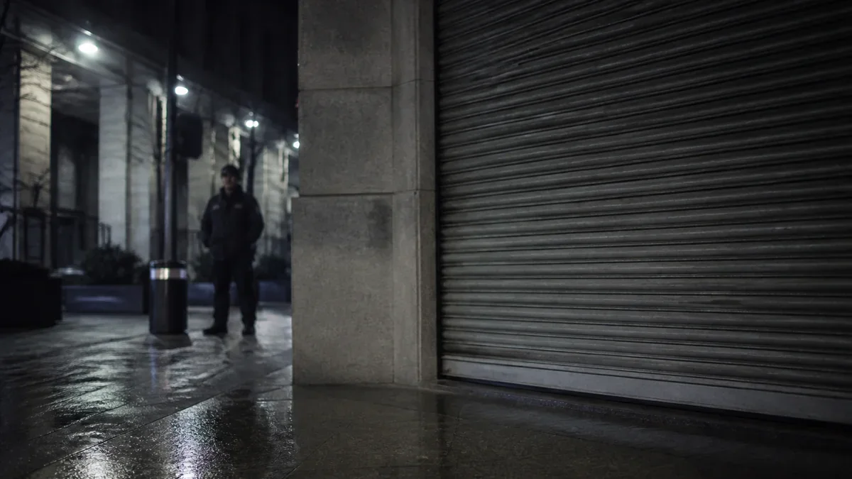Calle comercial de noche en Santiago con persiana cerrada y un guardia de seguridad al fondo